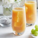 A glass of orange juice with ice cubes and grapes next to a bowl of Bossen White Grape Oolong Tea Bags.