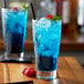 A glass of Monin blue raspberry drink with ice and raspberries.