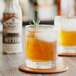 A glass of whiskey and a glass of beer on a table with a bottle of Fee Brothers Whiskey Barrel-Aged Bitters.