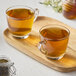 A wooden tray with two glass cups of Numi Moroccan Mint tea and a jar of honey.