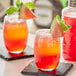 A glass of Finest Call watermelon puree with a drink on a table with a slice of watermelon on top.