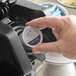 A hand holding a round Ellis Presidential Coffee single serve cup over a coffee maker.