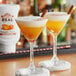 Two glasses of orange drinks garnished with cinnamon and orange on a table in a cocktail bar.