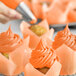 A person using a pastry brush to add orange frosting to cupcakes.