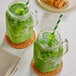 Two glass jars of green Matcha lattes with straws on a table.