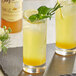 A glass of yellow liquid with a lemon slice and basil leaf next to a bottle of DaVinci Gourmet Lemonade Concentrate.