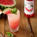 A glass of watermelon drink with a Monin Watermelon Flavoring syrup bottle in the background.