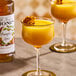 A glass of pumpkin spice-flavored beverage garnished with a flower, next to a bottle of Monin Premium Pumpkin Spice Flavoring Syrup.