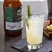 A glass of liquid made with 18.21 Bitters Spicy Ginger Beer Concentrated Syrup with a sprig of rosemary on top.