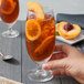 A hand holding a glass of iced tea with a peach slice.