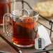 A glass mug of Numi Organic Emperor's Pu-Erh Tea with a tea bag in it on a white tray.