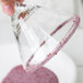 A hand rimming a glass with pink Rokz Pomegranate Cocktail Rimming Sugar.