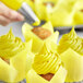 A hand using yellow Chefmaster food coloring to swirl yellow frosting on a cupcake.