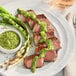 A plate of meat and asparagus with a bowl of Regal Chimichurri seasoning.