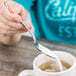 A hand holding a Oneida Rosewood stainless steel teaspoon pouring sugar into a cup of tea.