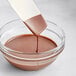 A spoon pouring Cacao Barry Brune Pate a Glacer compound coating into a bowl.