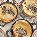 A table set with a pancake topped with blueberries and powdered sugar with a fork on a cloth next to a pan of blueberries.