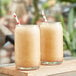 Two glasses of brown liquid with straws on top of a wooden board.