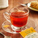 A glass cup of Bigelow Perfect Peach tea with a tea bag on a saucer.