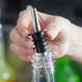 A person using a metal tip to pour Regal Cocktail Sweet and Sour Mix into a glass bottle on a counter.