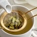 A white pitcher pouring cardamom pods into a strainer.