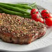 A piece of meat seasoned with Regal Canadian Steak Seasoning on a plate with green beans and tomatoes.