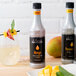 A white Monin Mango Concentrated Flavor bottle next to a glass of mango liquid on a table.