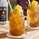 A mason jar filled with iced tea garnished with mango chunks and mint, served with a straw.