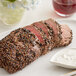 A piece of meat seasoned with Regal Cracked Black Pepper on a plate with white sauce and a glass of wine.