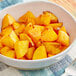 A bowl of food with yellow potatoes and a fork on a white table.