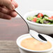 A hand holding a Oneida heavy weight oval bowl soup spoon over a bowl of soup.