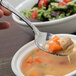 A Oneida Bague stainless steel oval bowl soup spoon holding soup over a bowl.