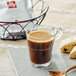 A glass cup of illy coffee next to a basket of coffee.