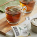 A glass cup of Numi Organic Hojicha Tea with a tea bag in it on a wooden board.