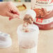 A hand pouring Premier Protein chocolate protein powder into a white container.