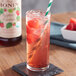 A glass of red drink with Monin Organic Raspberry Fruit Syrup, ice, and a straw.