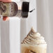 A hand pouring UPOURIA Cookies & Cream topping onto a coffee drink.