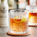 A glass of whiskey with a lemon garnish next to a bottle of Fee Brothers Old Fashioned Aromatic Bitters.