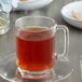 A glass mug of brown Earl Grey tea on a plate.