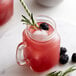 A glass mug of blackberry lemonade with a straw sitting on a white table next to a Monin Blackberry Fruit Puree jar.