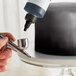 A person using a silver Chefmaster airbrush to spray a cake.