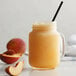 A glass of peach smoothie with peach slices on a table.