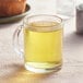 A glass mug of yellow Davidson's Organic Genmaicha tea sits on a table.
