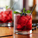 A glass of red Huckleberry flavored drink with ice and berries on a table in a cocktail bar.