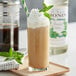 A glass of brown liquid topped with whipped cream and a mint leaf.