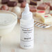 A white bottle of Chefmaster white oil-based candy color with a white cap next to a bowl of white liquid.