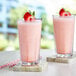 Two glasses of Capora strawberry smoothie with straws on a marble surface.