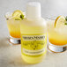A bottle of Nielsen-Massey Pure Lemon Extract next to two glasses of lemonade with lemon wedges.