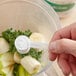 A hand using a measuring spoon to add Add A Scoop Calcium Blend supplement powder to a blender.