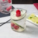 A glass of water with raspberry and cucumber slices on a white background.